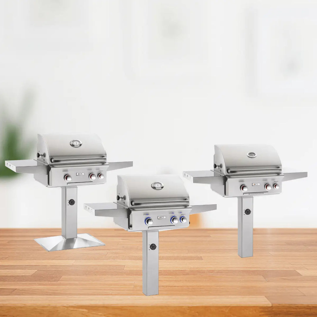 AOG post mount grills collection with stainless steel gas grills on pedestal bases, featuring side shelves and control knobs for outdoor cooking.