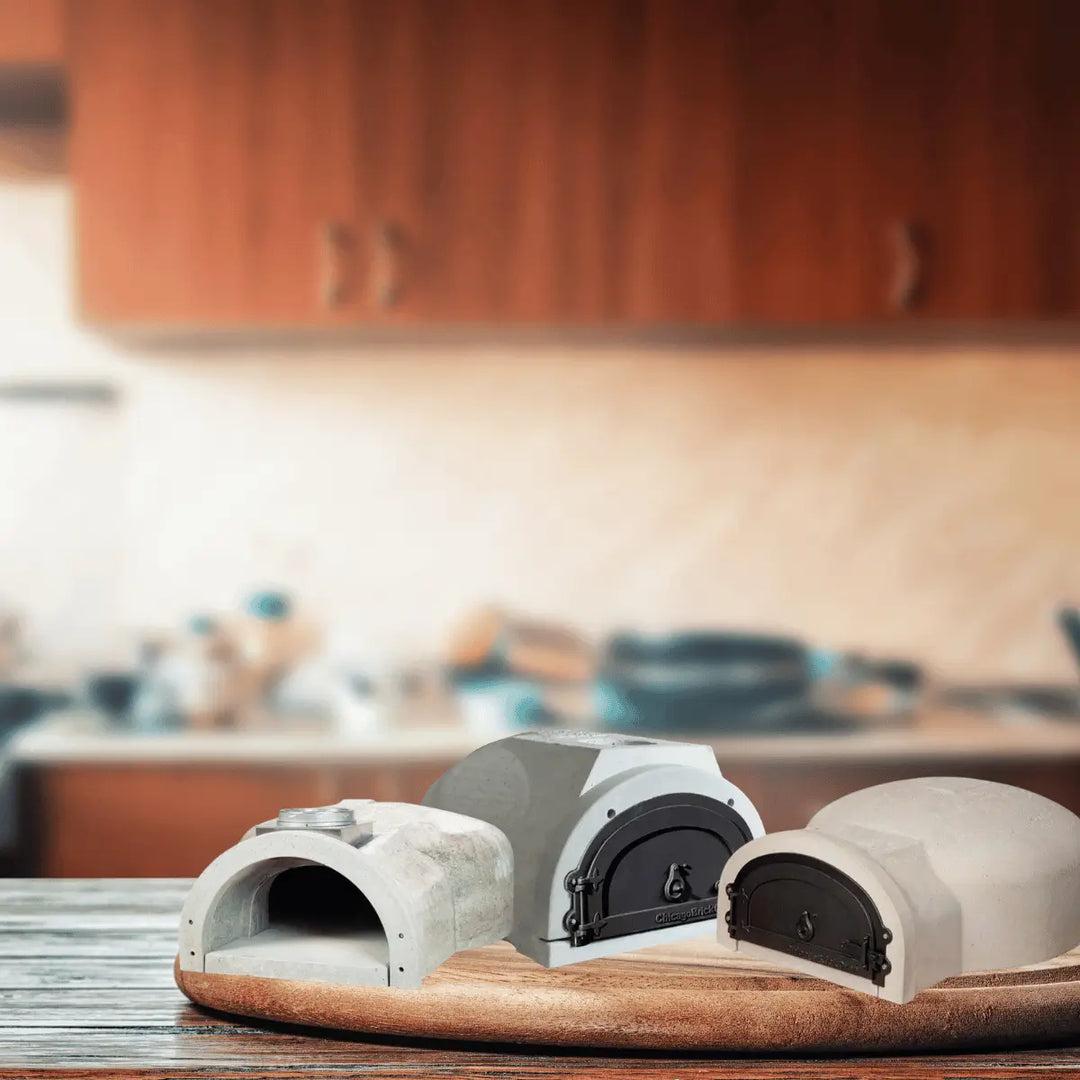 Chicago Brick Oven DIY pizza oven kits with concrete shells and metal doors, displayed on a wooden surface in a modern kitchen setting