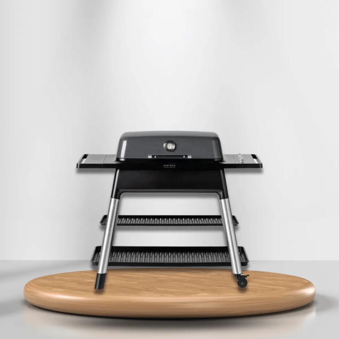 Everdure gas grill with side shelves and temperature gauge, sleek black outdoor grill on wooden platform for modern cooking setup