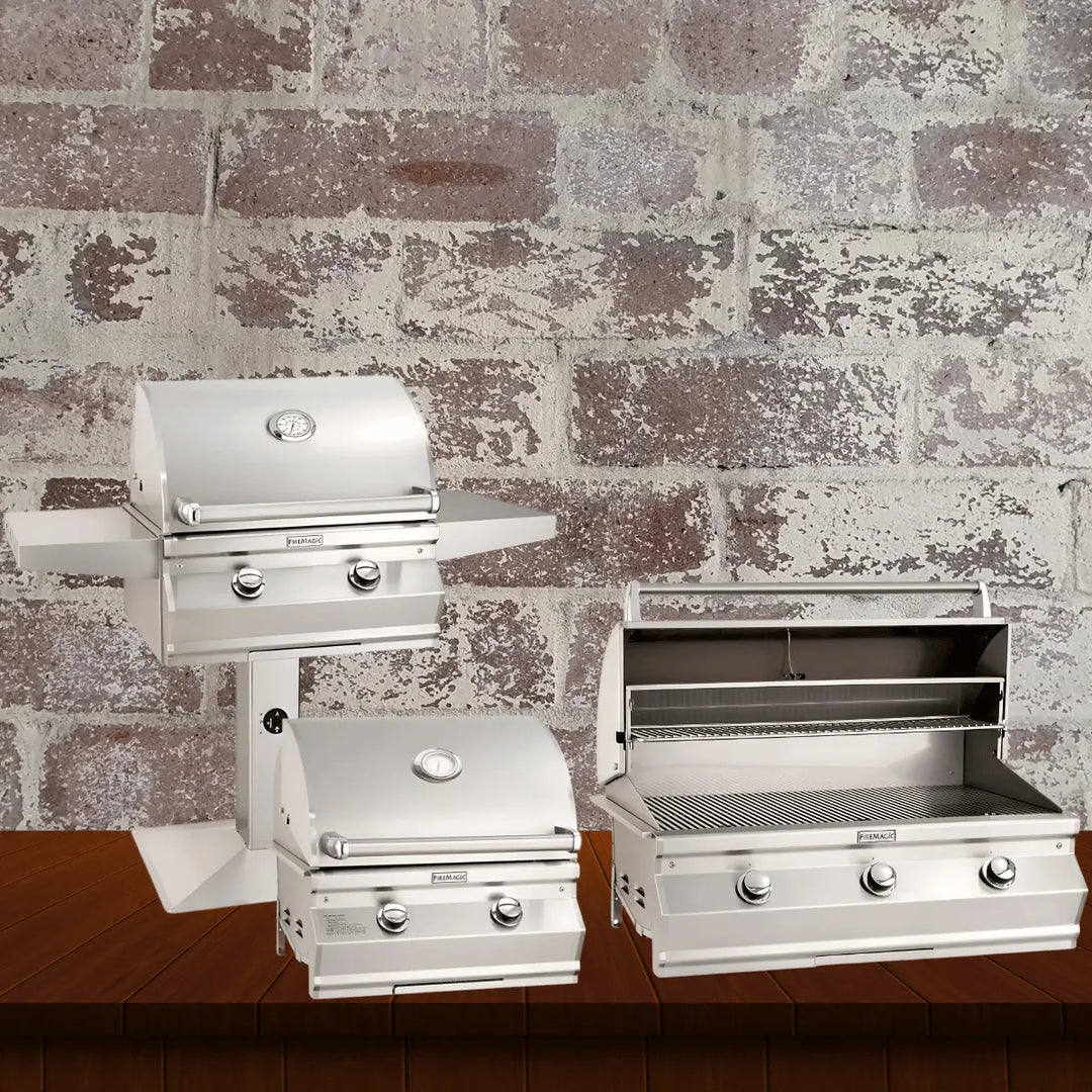 Fire Magic Choice Multi-User Series collection featuring durable stainless steel gas grills, including pedestal-mounted and built-in models with simple controls and open grilling surfaces, displayed on a wooden surface with a rustic brick wall background.