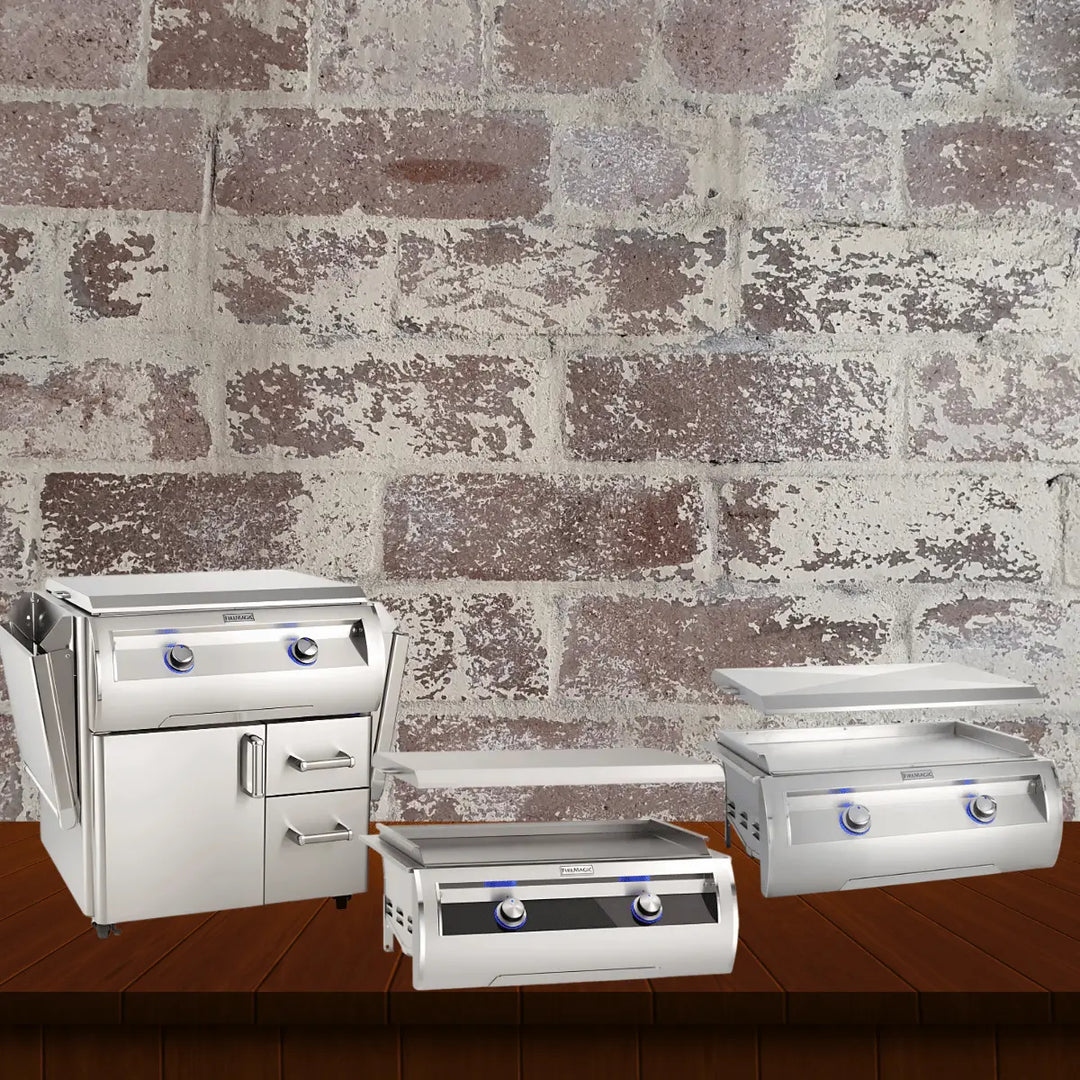 Fire Magic gourmet griddles collection featuring stainless steel outdoor griddles, including built-in and cart-style models with flat-top cooking surfaces and dual control knobs, displayed on a wooden surface with a rustic brick wall background.