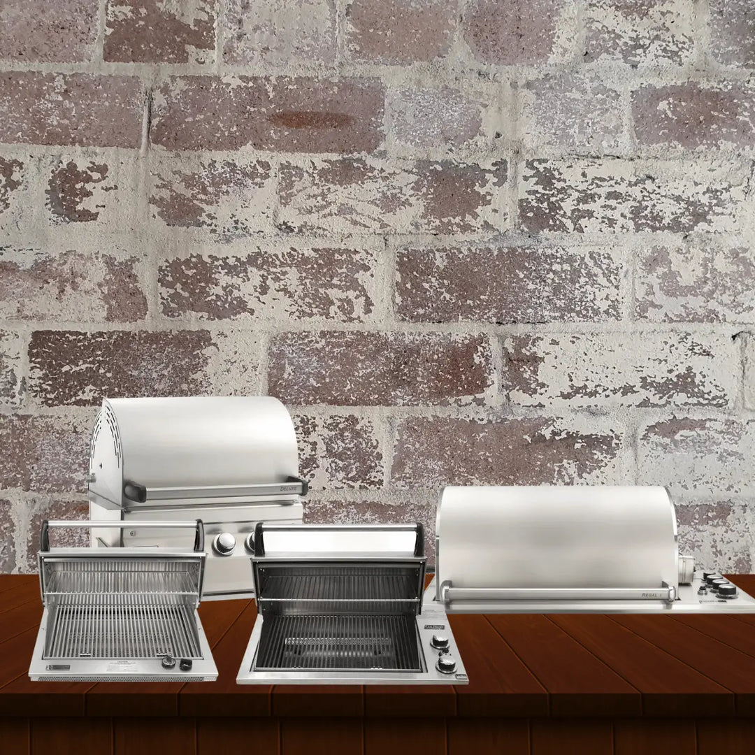 Fire Magic Legacy Series grills collection featuring stainless steel gas grills, including built-in and countertop models with open lids and grilling grates, displayed on a wooden surface with a rustic brick wall background.